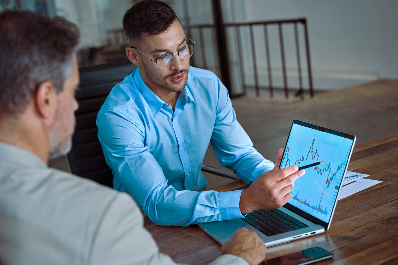 Financial advisor explaining invest stock market data consulting investor. Two busy business men analysts doing finance trading analysis pointing at exchange chart on laptop screen working in office.