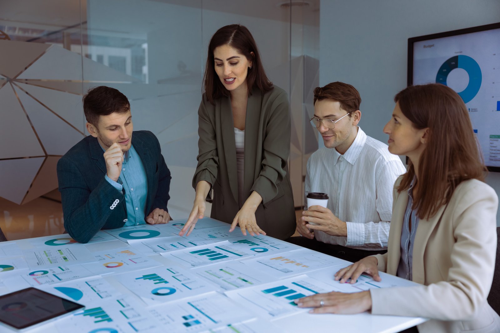 Young Latin businesswoman presenting product sales analytic data to team of colleagues. Professional analysts discussing paper marketing report, brainstorming on project growth strategy